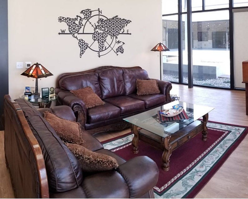 May include: A living room with two brown leather sofas, a glass-top coffee table, and a rug. The wall behind the sofas has a metal world map with a compass design.