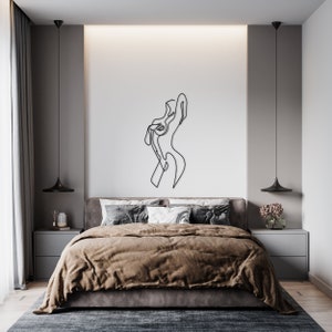 May include: A black and white line drawing of a person's body in a modern minimalist style. The drawing is on a white wall above a brown bed with white pillows.