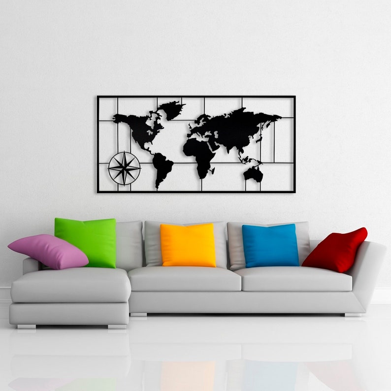 May include: A black metal wall decor featuring a world map with a compass in the bottom left corner. The map is displayed on a white wall above a gray sectional sofa with colorful throw pillows.