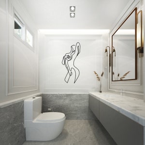 May include: A white toilet with a closed lid in a modern bathroom with a marble countertop and a large mirror. A black line drawing of a woman is on the wall above the toilet.