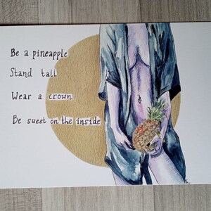 Pode incluir: Impressão de arte em aquarela com uma figura segurando um abacaxi. A obra de arte inclui o texto: "Seja um abacaxi, Fique de pé, Use uma coroa, Seja doce por dentro". O fundo tem um círculo dourado.