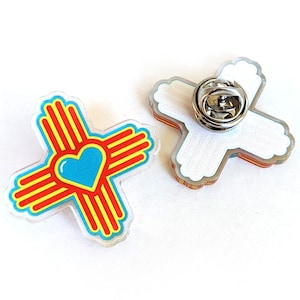 May include: A red, yellow, and blue pin with a heart in the center. The pin is shaped like a cross and has a silver pin back.