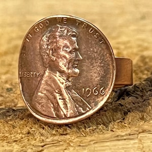 May include: A copper penny ring featuring a 1966 Lincoln penny with the inscription "In God We Trust" and "Liberty".