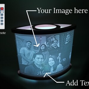 May include: A white, cylindrical lamp with a black base and a clear acrylic panel displaying a family photo. The lamp has a remote control with multiple colour options. The text "Your Image here" and "Add Text" are written on the image.