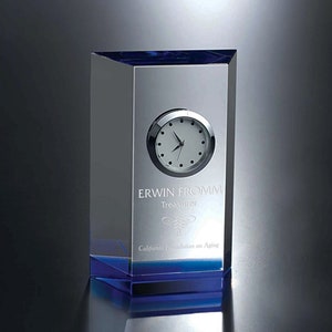 May include: A clear glass clock with a blue base. The clock face is white with black numbers and hands. The inscription reads "Erwin Fromm, Treasurer, California Foundation on Aging".