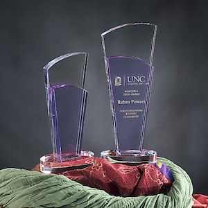 May include: Two clear glass awards with purple accents. The larger award has the text "UNC School of Law Winston R. Crisp Award Ruben Powers For Outstanding Student Leadership" on it. The smaller award is similar but does not have any text.