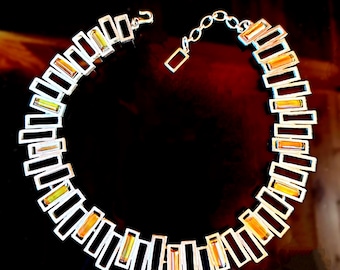 May include: A necklace featuring a series of rectangular links arranged in a circular pattern. The links alternate between solid black rectangles and translucent amber-colored rectangular stones set within silver-toned metal frames.