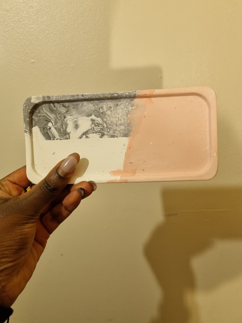 Op de afbeelding: Een rechthoekige dienblad met een marmerachtig grijs en wit ontwerp aan de ene kant en een effen lichtroze kleur aan de andere kant.