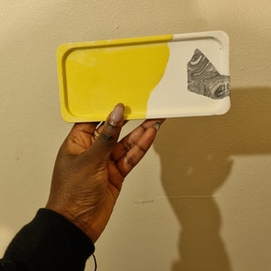 Op de afbeelding: Een klein rechthoekig dienblad met een geel en wit marmerpatroon. Het dienblad heeft een grijs marmeraccent aan de witte kant.