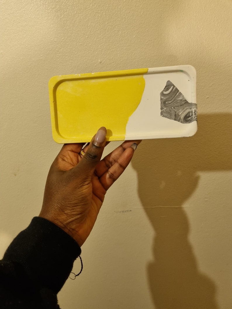 Op de afbeelding: Een klein rechthoekig dienblad met een geel en wit marmerpatroon. Het dienblad heeft een grijs marmeraccent aan de witte kant.