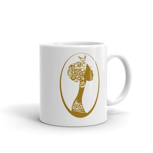 May include: White ceramic mug with a gold silhouette of a woman with an intricate hairstyle. The woman is facing to the right and is in an oval frame.