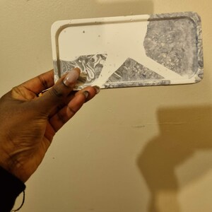 Op de afbeelding: Een rechthoekige witte en grijze dienblad met een marmerpatroon. Het dienblad heeft een verhoogde rand en is gemaakt van glad, duurzaam materiaal.