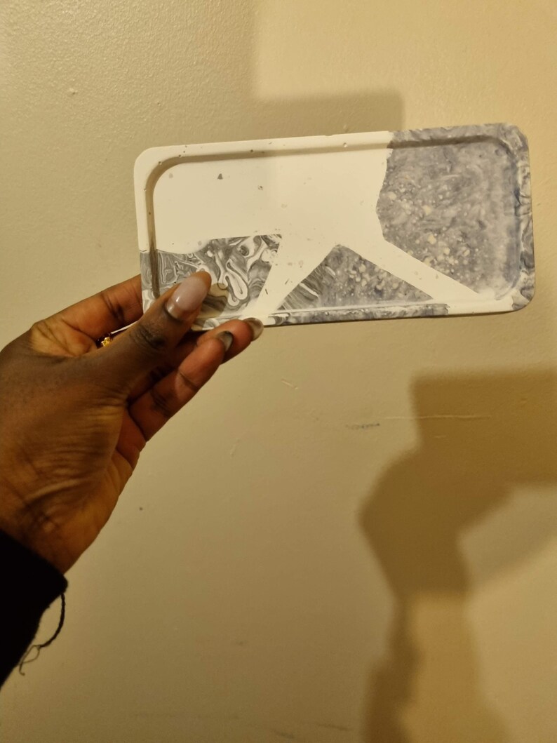 Op de afbeelding: Een rechthoekige witte en grijze dienblad met een marmerpatroon. Het dienblad heeft een verhoogde rand en is gemaakt van glad, duurzaam materiaal.