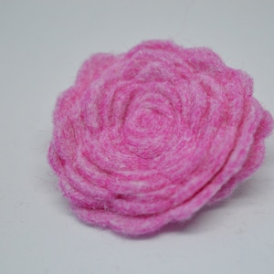 May include: A pink felt flower with a layered, rosette design. The flower is made of soft, fuzzy felt and has a delicate, feminine appearance.