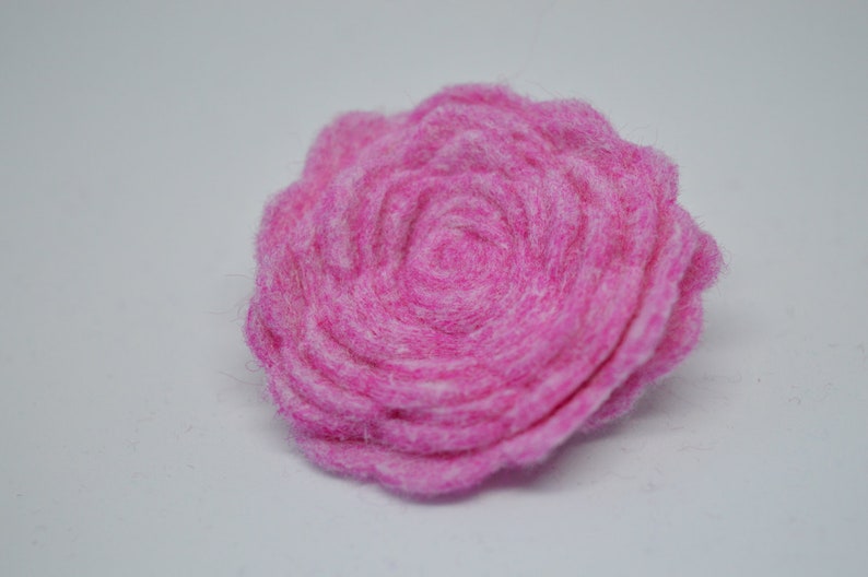 May include: A pink felt flower with a layered, rosette design. The flower is made of soft, fuzzy felt and has a delicate, feminine appearance.