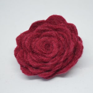 May include: A deep red felt rose flower. The rose is made of multiple layers of felt, creating a textured and dimensional look.