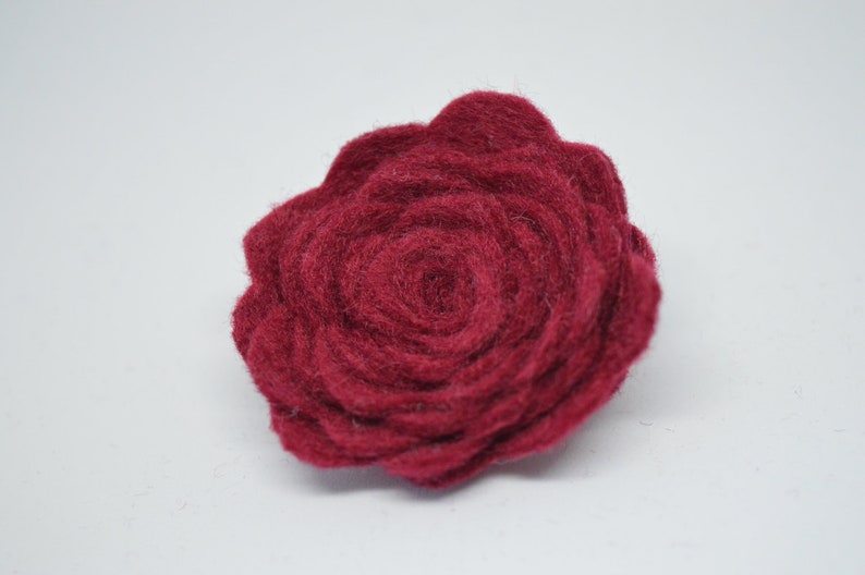 May include: A deep red felt rose flower. The rose is made of multiple layers of felt, creating a textured and dimensional look.