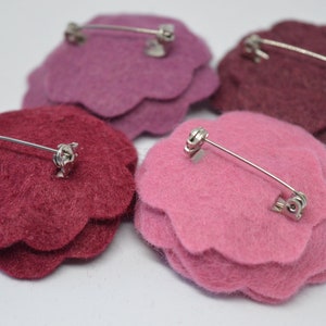 May include: Four felt flower brooches in pink, burgundy, and a darker shade of burgundy. Each brooch has a silver pin and clasp on the back.