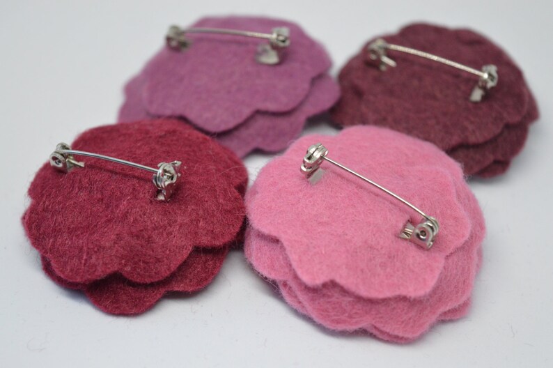 May include: Four felt flower brooches in pink, burgundy, and a darker shade of burgundy. Each brooch has a silver pin and clasp on the back.
