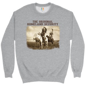 May include: A gray sweatshirt with the text "THE ORIGINAL HOMELAND SECURITY" printed on the front. The text is in a brown font. Below the text is a vintage image of two Native American men on horseback.