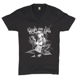 Puede incluir: Camiseta negra de cuello en V con un gráfico blanco de una mujer con un pañuelo en la cabeza fumando un cigarrillo y rodeada de hojas de marihuana. El texto "High on Life" está escrito en blanco sobre la mujer.