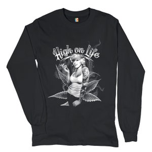 Puede incluir: Camiseta negra de manga larga con un gráfico blanco de una mujer fumando un cigarrillo con el texto "High on Life" encima de ella.