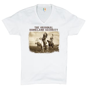 May include: White V-neck t-shirt with a vintage image of Native American men on horseback and the text "THE ORIGINAL HOMELAND SECURITY".