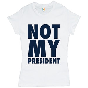 May include: White t-shirt with the text "NOT MY PRESIDENT" printed in dark blue.