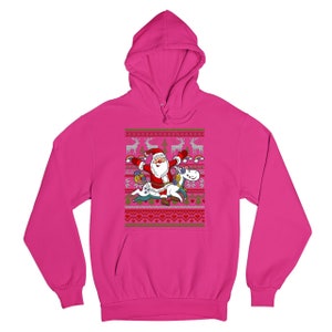 May include: A pink hooded sweatshirt with a Christmas-themed design featuring Santa Claus riding a unicorn. The design includes a festive pattern of snowflakes, reindeer, and hearts.