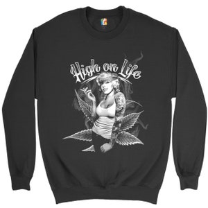Puede incluir: Sudadera negra con un gráfico blanco de una mujer fumando un cigarrillo con el texto "High on Life" encima de ella.