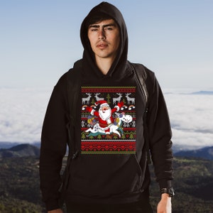 May include: A black hoodie with a Christmas-themed design featuring Santa Claus riding a unicorn. The design includes reindeer, rainbows, and snowflakes.