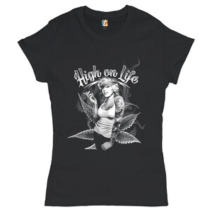 Puede incluir: Camiseta negra con un gráfico blanco de una mujer con un cigarrillo y hojas de marihuana. El texto "High on Life" está escrito en una fuente estilizada sobre la mujer.