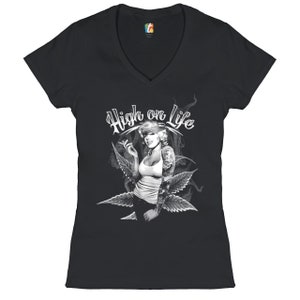 Könnte beinhalten: Schwarzes V-Ausschnitt-T-Shirt mit einem weißen Motiv einer Frau, die eine Zigarette mit Marihuanablättern raucht, und dem Text "High on Life".