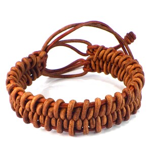 Puede incluir: Una pulsera de cuero marr&oacute;n con un dise&ntilde;o tejido. La pulsera est&aacute; hecha de m&uacute;ltiples hebras de cuero, creando una apariencia texturizada. Los extremos de la pulsera tienen lazos ajustables para un ajuste personalizado.