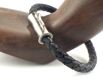 May include: A black leather bracelet with a silver magnetic clasp. The bracelet is braided and has a smooth, polished finish.