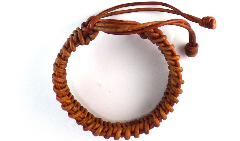 Puede incluir: Pulsera de cuero marr&oacute;n hecha a mano con un dise&ntilde;o tejido. La pulsera presenta un patr&oacute;n trenzado y lazos de cuero ajustables. El color marr&oacute;n c&aacute;lido y la textura sugieren una est&eacute;tica r&uacute;stica y natural. Circunferencia de unos 20 cm.