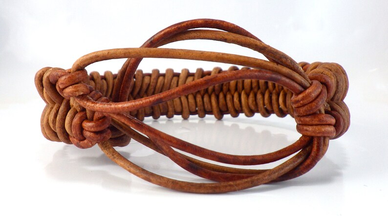 Puede incluir: Pulsera de cuero marr&oacute;n con una secci&oacute;n central trenzada y nudos decorativos. La pulsera est&aacute; hecha de m&uacute;ltiples cordones de cuero, creando un accesorio texturizado y elegante. El dise&ntilde;o incorpora una secci&oacute;n central de hebras de cuero muy tejidas.