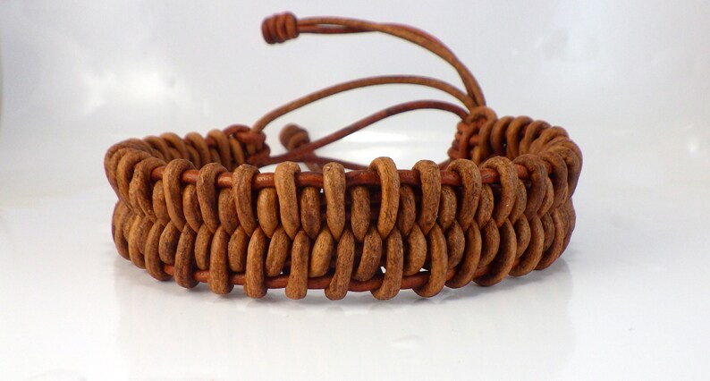 Puede incluir: Una pulsera de cuero marr&oacute;n con un dise&ntilde;o tejido. La pulsera presenta una construcci&oacute;n de doble capa con una serie de piezas de cuero redondeadas. Ajustable con un cord&oacute;n de cuero marr&oacute;n. Un accesorio artesanal.