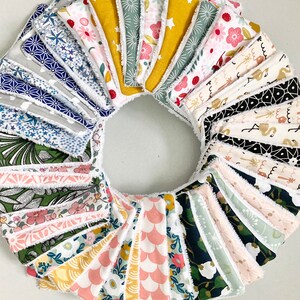 May include: A collection of 20 reusable makeup remover pads with various colorful patterns. The pads are made of soft fabric with a white, fluffy trim. The pads are arranged in a circle, with the patterns facing outwards.