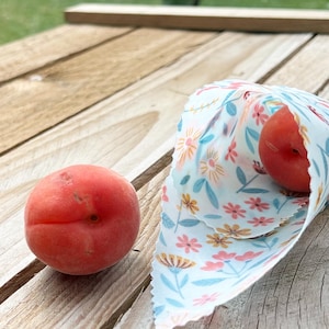 May include: Two red apricots, one wrapped in a white fabric with a floral pattern, and the other on a wooden surface.