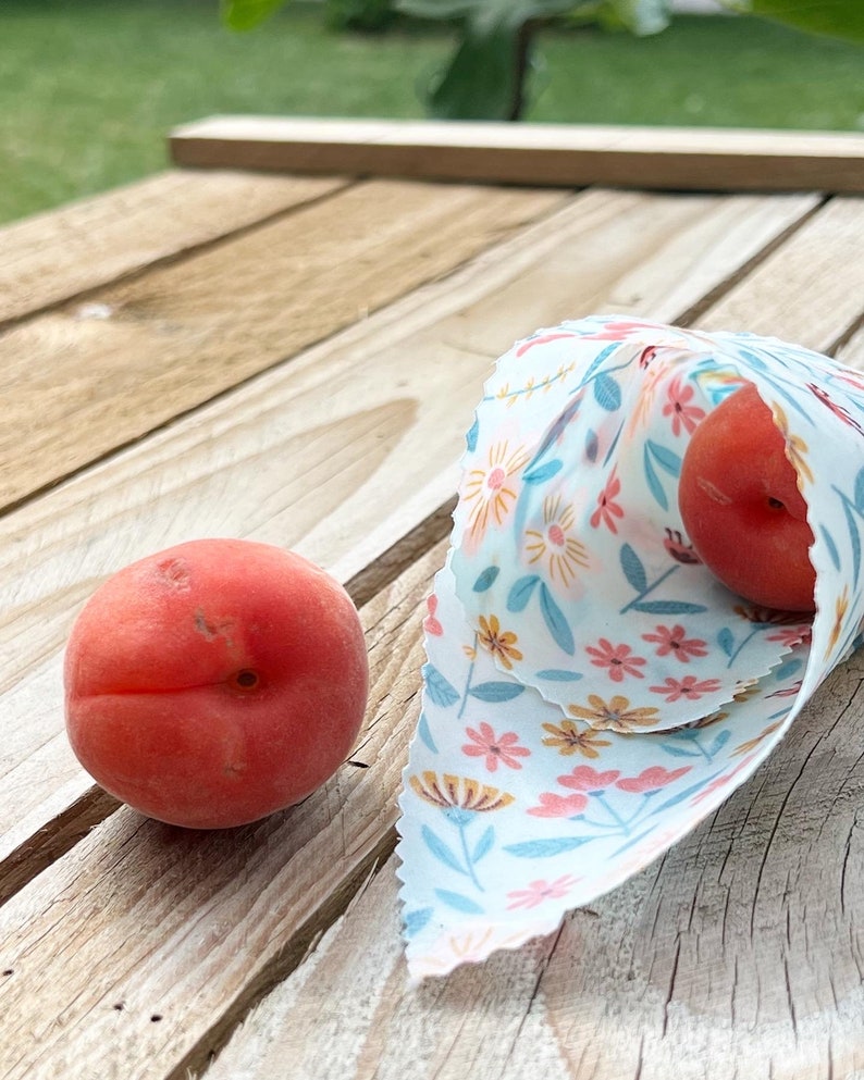 May include: Two red apricots, one wrapped in a white fabric with a floral pattern, and the other on a wooden surface.
