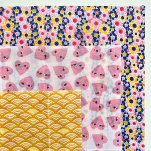May include: A collection of patterned fabric squares. The top fabric features a pink floral design with yellow and blue accents. Below, a white fabric with pink heart shapes is visible. The bottom fabric has a yellow, wave-like pattern.