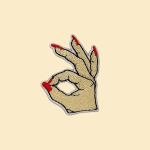 Könnte beinhalten: Gestickter Bügel-Patch einer Hand, die das OK-Zeichen mit rotem Nagellack zeigt.