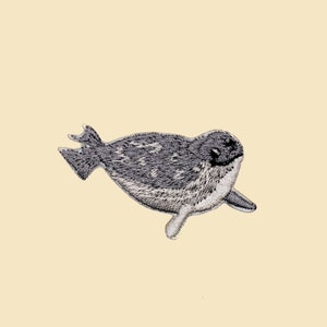 Könnte beinhalten: Ein gestickter Aufnäher, der ein schwimmendes Seehündchen in Grau und Weiß zeigt. Der Seehund blickt nach rechts und hat eine dunkelgraue Nase und Augen.