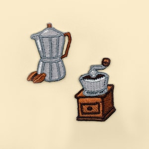 Op de afbeelding: Twee geborduurde patches, een van een zilveren koffiepot en de andere van een zilveren koffiemolen met een bruine basis.