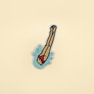 May include: An embroidered patch of a person diving into water, wearing a red bikini bottom. The water is depicted in blue and the person's legs are tan.