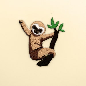 May include: Embroidered patch of a brown sloth hanging from a branch with green leaves.