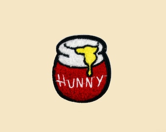 May include: Red and white embroidered iron-on patch of a honey pot with the word "Hunny" on the front.