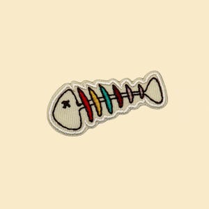 May include: White embroidered patch of a fish skeleton with a red, orange, yellow, green, blue, and purple spine.