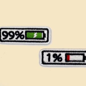 May include: Two embroidered iron-on patches depicting battery icons. One patch shows a battery icon with a green bar and the text "99%". The other patch shows a battery icon with a red bar and the text "1%".